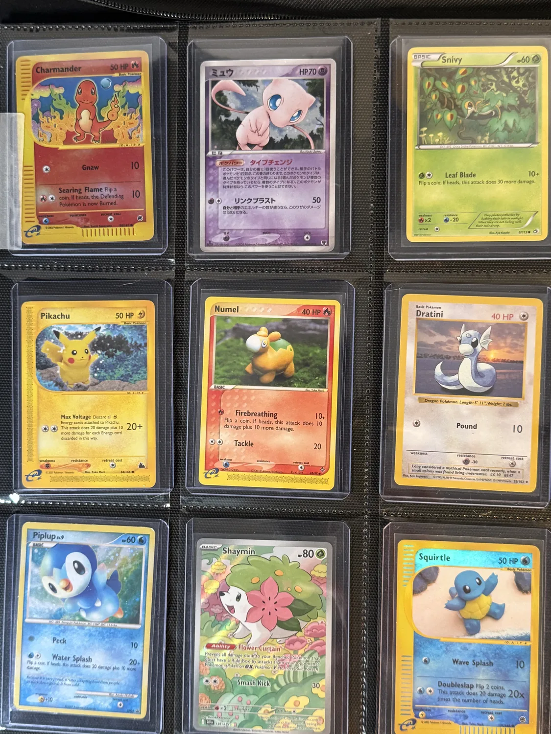 Nine-pocket page of mostly vintage cards — Charmander, Mew, Snivy, Pikachu, Numel, Dratini, Piplup, Shaymin and Squirtle in open outdoor settings