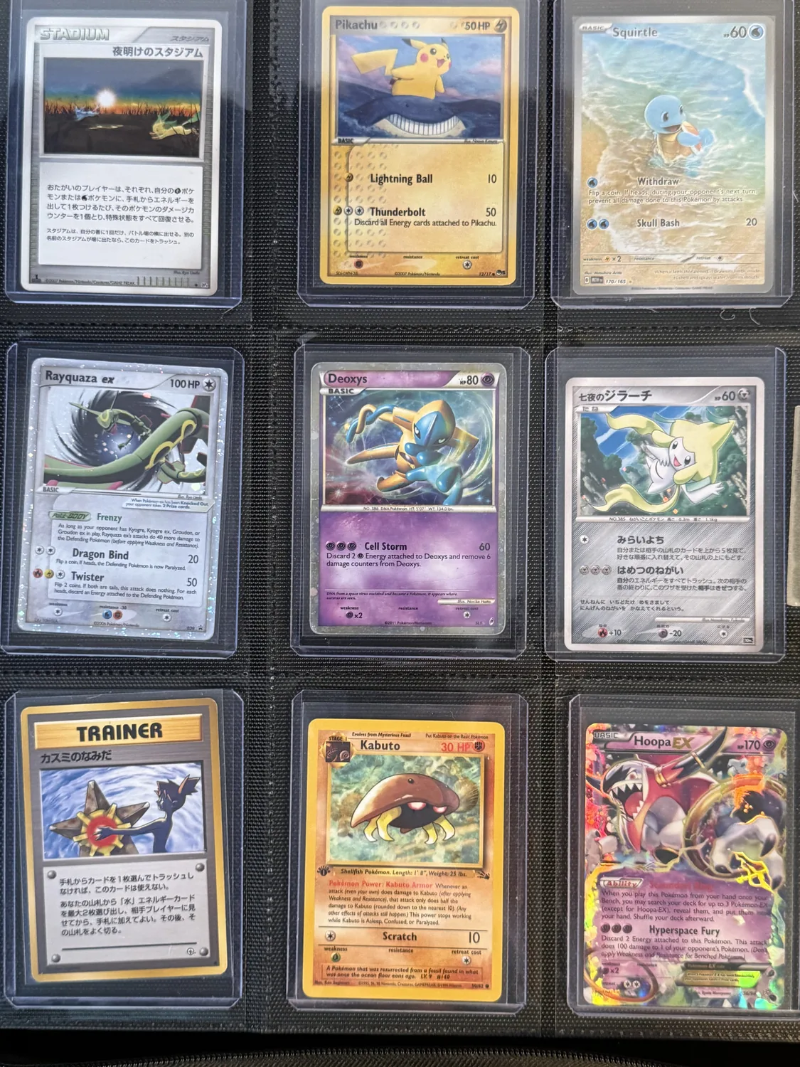 Nine-pocket page of edges and crossings — a sunrise stadium, Squirtle at a shoreline, Deoxys and Rayquaza in open space, a revived Kabuto fossil, and Hoopa's portal rings